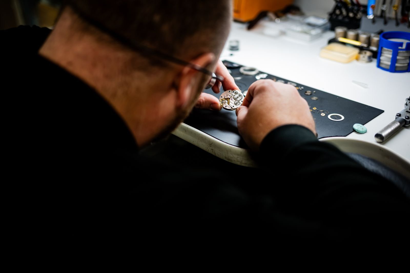 Watchmaker inspecting a mechanical wristwatch with precision tools at a workbench