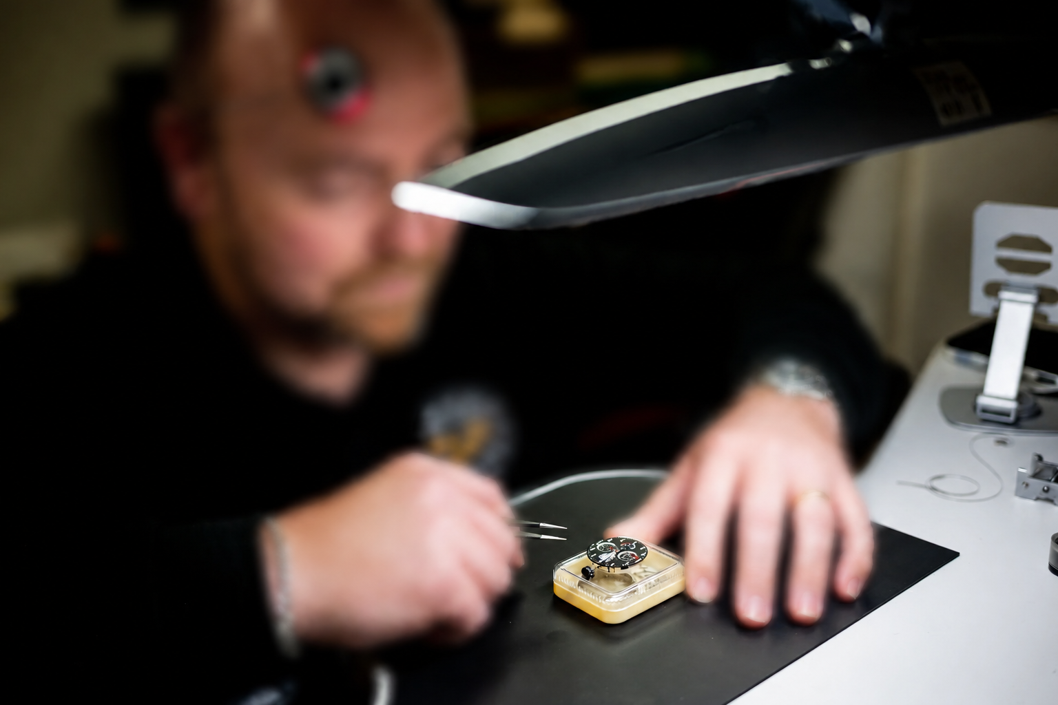 Skilled watchmaker examining a wristwatch under a bright bench lamp
